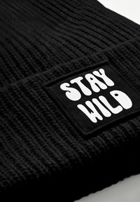 Black knitted beanie featuring a textured pattern and a rectangular black patch with the text "STAY WILD" in bold white letters.