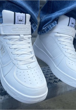 White high-top sneakers with textured leather material, perforated toe, and prominent branding on the tongue and side. Accented with a strap.