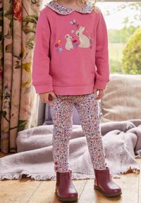 Różowy sweatshirt z haftowanymi królikami i kwiatami, legginsy w kwiaty oraz burgundowe botki za kostkę. Miękka tkanina i krój z okrągłym dekoltem.