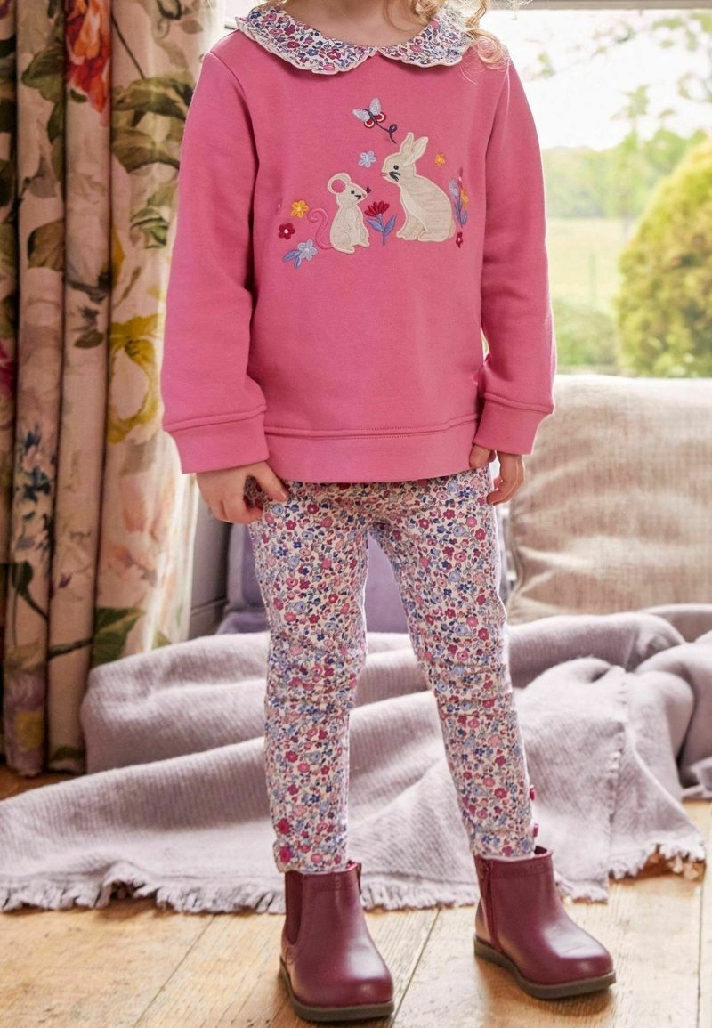 Różowy sweatshirt z haftowanymi królikami i kwiatami, legginsy w kwiaty oraz burgundowe botki za kostkę. Miękka tkanina i krój z okrągłym dekoltem.