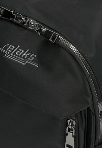 Zaino in nylon nero con design curvo, caratterizzato da una cerniera argentata, accessori lucidi e logo in rilievo nella parte anteriore.