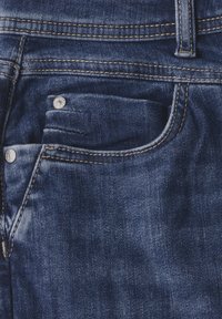 Granatowe dżinsy z przodu z kieszenią zapinaną na srebrny guzik, kontrastującym żółtym przeszyciem i lekko wyblakłą fakturą materiału.