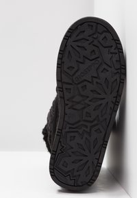 Semelle de chaussure en caoutchouc noir présentant un motif géométrique en forme de flocon de neige, avec un marquage en relief et une surface texturée pour une meilleure adhérence.