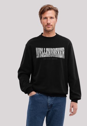 Schwarzer Sweatshirt mit Rundhalsausschnitt, versehen mit einem großen weißen grafischen Text "WELLENBREKER" und kleinerem Text darunter. Kombiniert mit blauen Jeans.