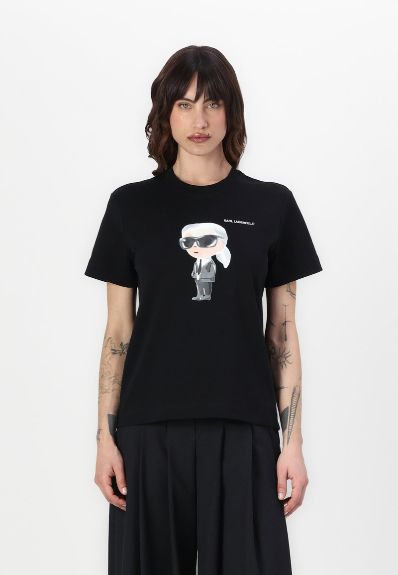 Juodas medvilninis marškinėliai su animacine grafika, vaizduojančia figūrą su akinių nuo saulės ir kostiumu, virš iliustracijos užrašyta "KARL LAGERFELD".