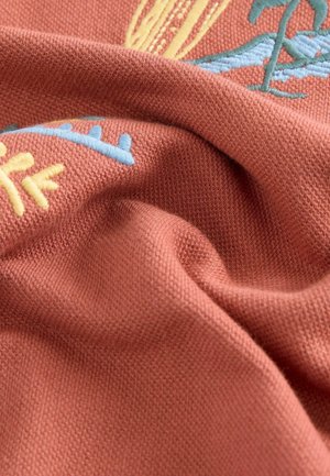 Tissu brodé avec un fond texturé corail et des motifs botaniques bleus et jaunes, mettant en valeur des détails complexes et une douceur remarquable.