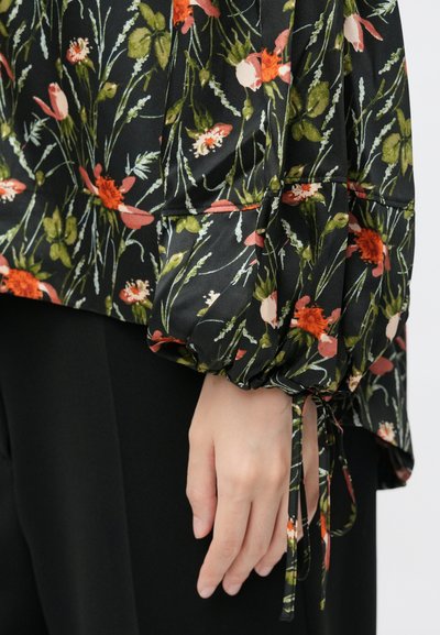 Gėlių bliuska su juodu pagrindu ir spalvingomis gėlėmis, pūkuotos rankovės ir surišimo detalė ties riešais. Lengvas, tekstūruotas audinys.