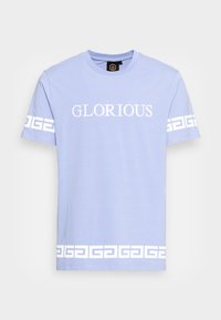 Camiseta de color azul claro hecha de algodón, con el texto "GLORIOSO" en blanco y patrones geométricos blancos en las mangas y el dobladillo.