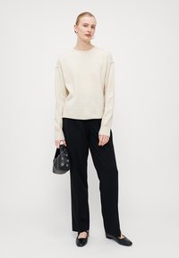 Maglione crema morbido con collo rotondo, vestibilità rilassata, abbinato a pantaloni neri a gamba larga e scarpe nere flat. Piccola borsa nera con occhielli.