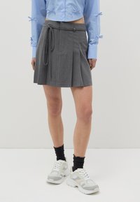 Falda gris con plisados y un lazo a juego en la cintura, hecha de una tela suave. Combinada con una camiseta corta azul claro y zapatillas blancas.