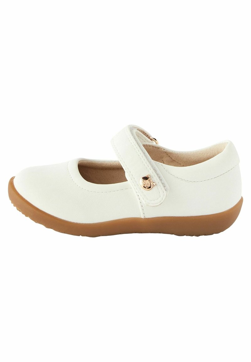 Chaussure Mary Jane blanche en cuir avec un bout arrondi, semelle plate en caoutchouc marron, bride ajustable et accent métallique circulaire.