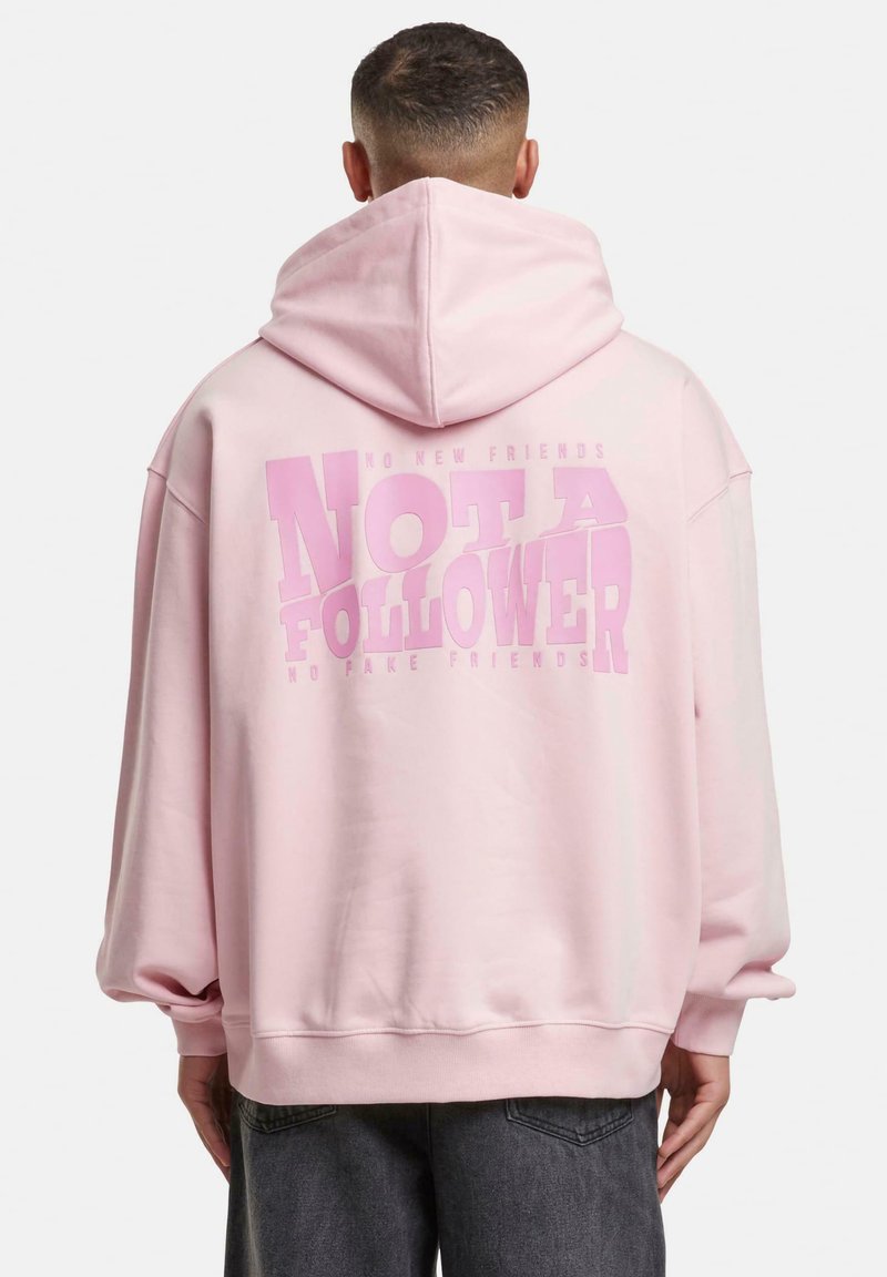 Sweat à capuche rose clair avec un grand motif imprimé au dos portant l'inscription « PAS UN SUIVANT ». Comprend une capuche, une coupe décontractée et des poignets côtelés.