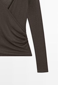 Haut à manches longues marron foncé style portefeuille avec un détail froncé d’un côté près de la taille, en tissu tricoté doux.