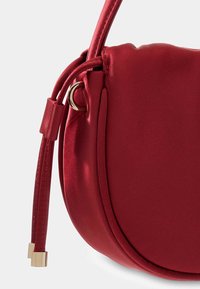 Czerwona satynowa torebka o zaokrąglonym kształcie, miękkiej strukturze i pojedynczym pasku na ramię z akcentami w kolorze złotym.