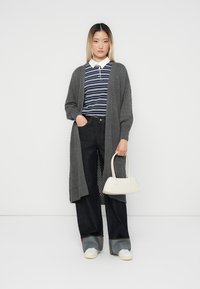Grauer gestrickter Cardigan mit strukturiertem Muster, navyblaues und weißes gestreiftes Hemd, dunkle Jeans, weiße Handtasche und weiße Turnschuhe.
