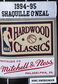 Toppa con la scritta "1994-95 SHAQUILLE O'NEAL" in nero. Il design include "HARDWOOD CLASSICS" con un pallone da basket e il logo NBA. Colori beige, rosso e blu.