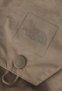 Țesătură maro cu o suprafață texturată, având un logo gri reliefat "THE NORTH FACE" și un buton circular cu text embossat.