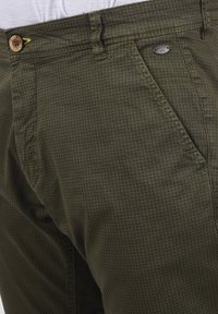 Olivengrønne bukser lavet af bomulds-twill, med et diskret stjernebånd, en knaplukning, og et mærke med brandnavnet på taljen.