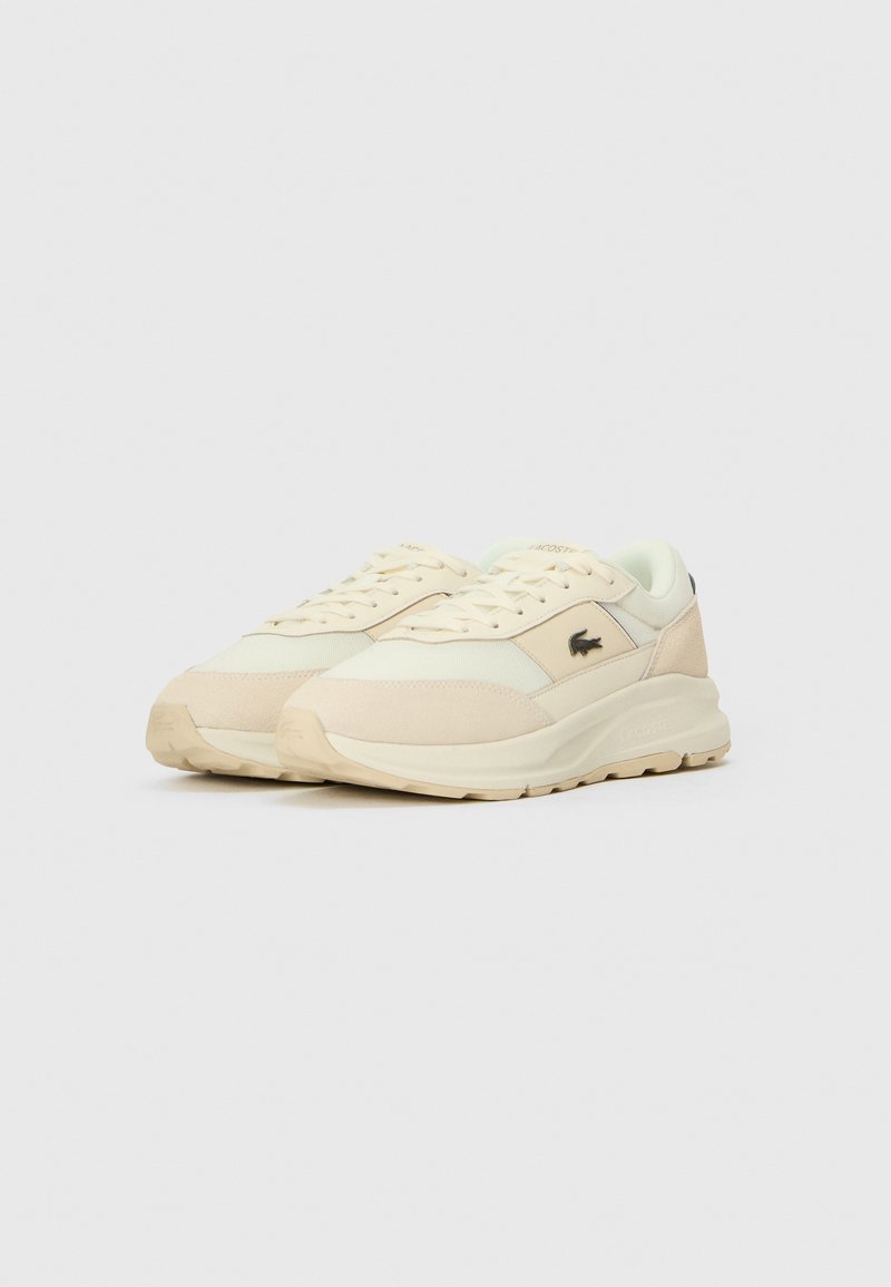 Beige Sneaker aus einer Mischung aus glattem Stoff und Wildlederakzenten, mit einer dicken Sohle und einem schwarzen Markenlogo an der Seite.