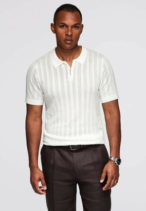Polo a maniche corte con colletto zip in bianco, caratterizzato da un motivo a righe verticali. Indossato con pantaloni marroni, con una texture liscia e una vestibilità slim.