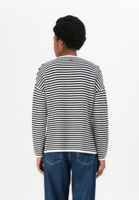 Camisa de manga longa às riscas pretas e brancas com decote redondo, corte descontraído e tecido suave. Combinada com jeans escuros.