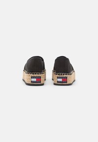 Czarne espadryle z płótna z plecionymi jucianymi podeszwami, z czerwoną, białą i niebieską naszywką na pięcie. Prosty, zakładany design.