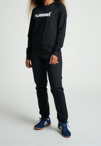 Sweat-shirt noir avec le logo "hummel", associé à un pantalon noir. Caractéristiques : coupe décontractée et chaussures de sport bleues avec des accents blancs.