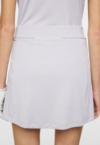 Ljusgrå idrottskjol gjord av mjukt tyg, med ett brett midjeband, en rundad nederkant och en liten logotyp broderad på baksidan.