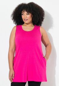 Top tunica senza maniche di un brillante colore rosa, realizzato in morbido tessuto, con scollatura rotonda e tasche laterali, indossato sopra leggings neri.