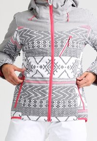 Grau gemusterte Jacke mit einem geometrischen Design in Schwarz und Weiß, mit rosafarbenen Akzenten, einem Frontreißverschluss und Seitentaschen.