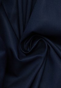 Tessuto blu navy con una superficie liscia e testurizzata, disposto in una piega a spirale, che mette in mostra il drappeggio e la flessibilità del tessuto.