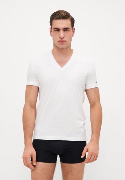 Weißes kurzärmliges V-Ausschnitt-T-Shirt aus glattem Baumwollstoff, taillierte Passform. Model trägt schwarze Boxershorts und steht vor einem hellen Hintergrund.