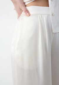 Crème-kleurige wijde broek met een gladde, lichte stof, voorzien van een geplooide voorkant en een platte tailleband.