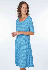 Kleid mit blauem Muster, quadratischem Ausschnitt, kurzen Ärmel und weitem Saum. Der Stoff weist ein geometrisches Design in verschiedenen Blautönen auf.