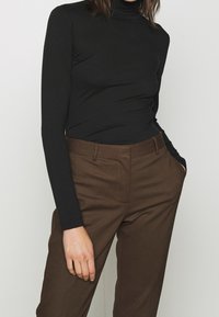 Svart långärmad polotröja i ett töjbart tyg, kombinerad med bruna skräddarsydda byxor med fickor och rak benmodell.