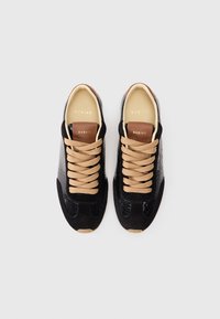 Czarne sneakersy z chropowatą skórą i zamszowym wierzchem, z beżowymi sznurówkami i brązowym skórzanym językiem z wytłoczonym logo.