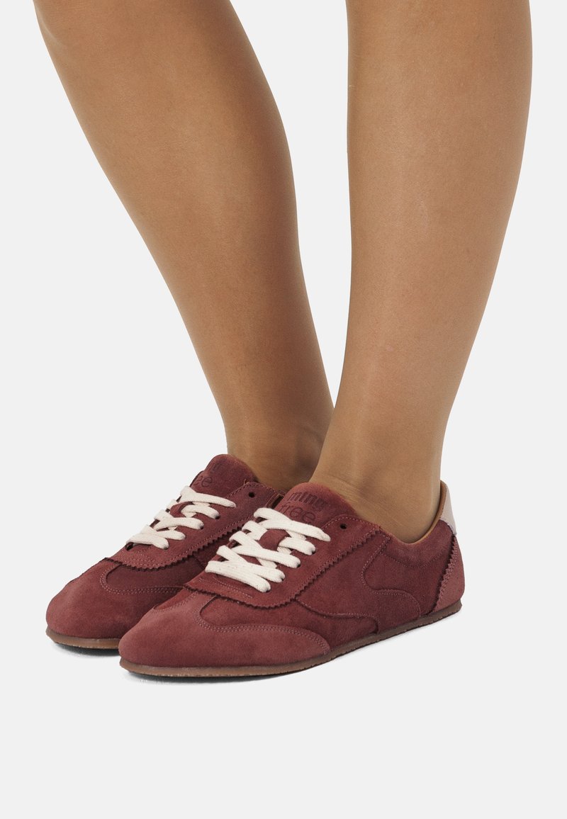 Sneakers in suede bordeaux con lacci bianchi, punta tondeggiante e dettagli in beige sul tallone. Presentano un design atletico classico e una superficie texture.