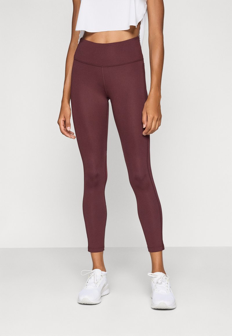 Burgundy leggings with a high waist, smooth texture, and fitted design. Paired with white athletic shoes and a cropped white top.