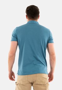 Polo shirt teal a maniche corte con colletto, realizzato in tessuto leggero. Texture liscia e spacchi laterali per facilitare i movimenti.