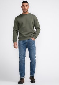 Olijfgroene sweatshirt met ronde hals, gecombineerd met lichtblauwe jeans en bruine veterschoenen. Glad materiaal met ribbelmanchetten en -zoom.
