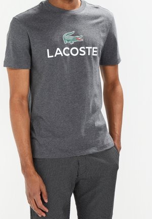 Grå bomulds t-shirt med et grønt krokodillelogo og "LACOSTE" tekst i hvid, med en klassisk rund halsudskæring og korte ærmer.