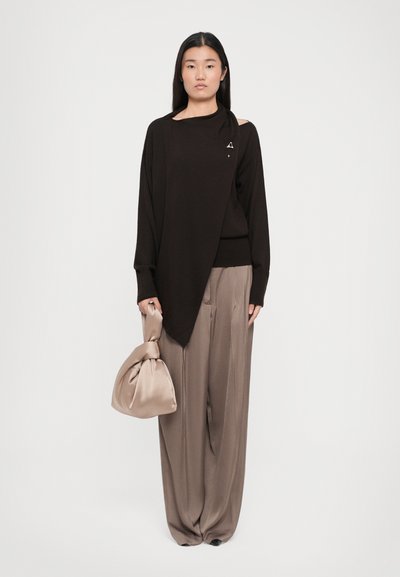 Brown asymmetrical sweater in smooth fabric, paired with pleated beige trousers, held with a beige knotted handbag.