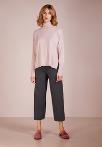 Svijetlo ružičasti turtleneck džemper s opuštenim krojem, uparen s tamno sivim hlačama širokih nogavica. Cipele su ružičaste s teksturiranim dizajnom.