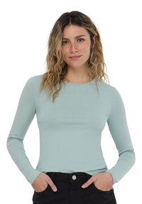 Maglietta aderente a maniche lunghe in morbido jersey blu chiaro. Collo rotondo, texture liscia e design minimalista. Abbinata a pantaloni neri.