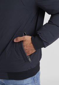 Marinejacke aus einem glatten, strukturierten Stoff; verfügt über eine Reißverschlusstasche an der Seite sowie gerippte, strukturierte Bündchen.