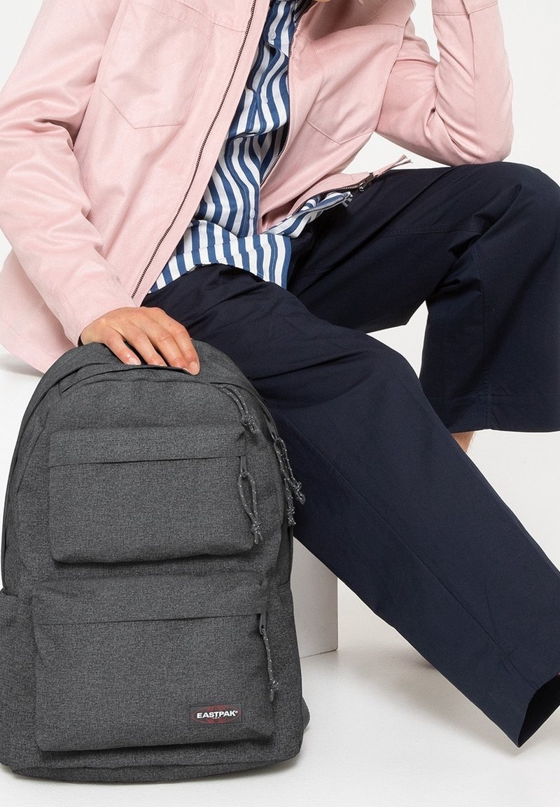 Gray Eastpak backpack with textured fabric, two front pockets, and logo patch. Features drawstring details and a rounded shape.