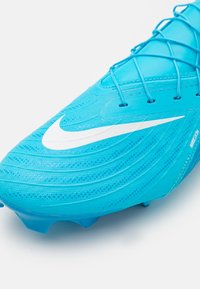 Turkusowy but piłkarski z teksturowaną syntetyczną cholewką, białym logo Nike oraz skomplikowanym systemem sznurowania. Podeszwa z kolcami zapewniająca przyczepność.