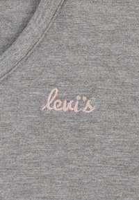 Sivi pulover s tkanino v v-izrezu. Ima roza vezeno "levi's" logo na prsih. Mehka tekstura, sproščen slog.