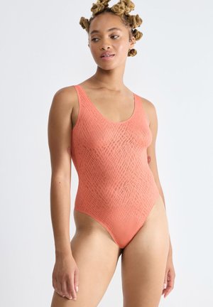 Koraalrode tankini met een rond uitgesneden halslijn, gemaakt van transparant textiel met een diamanten patroon en hoge beenopeningen.