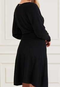 Schwarzes Strickkleid mit langen Ärmeln, taillierter Taille und ausgestelltem Rock. Verfügt über ein dezentes Rückendetail, eine glatte Textur und einen mittellangen Schnitt.
